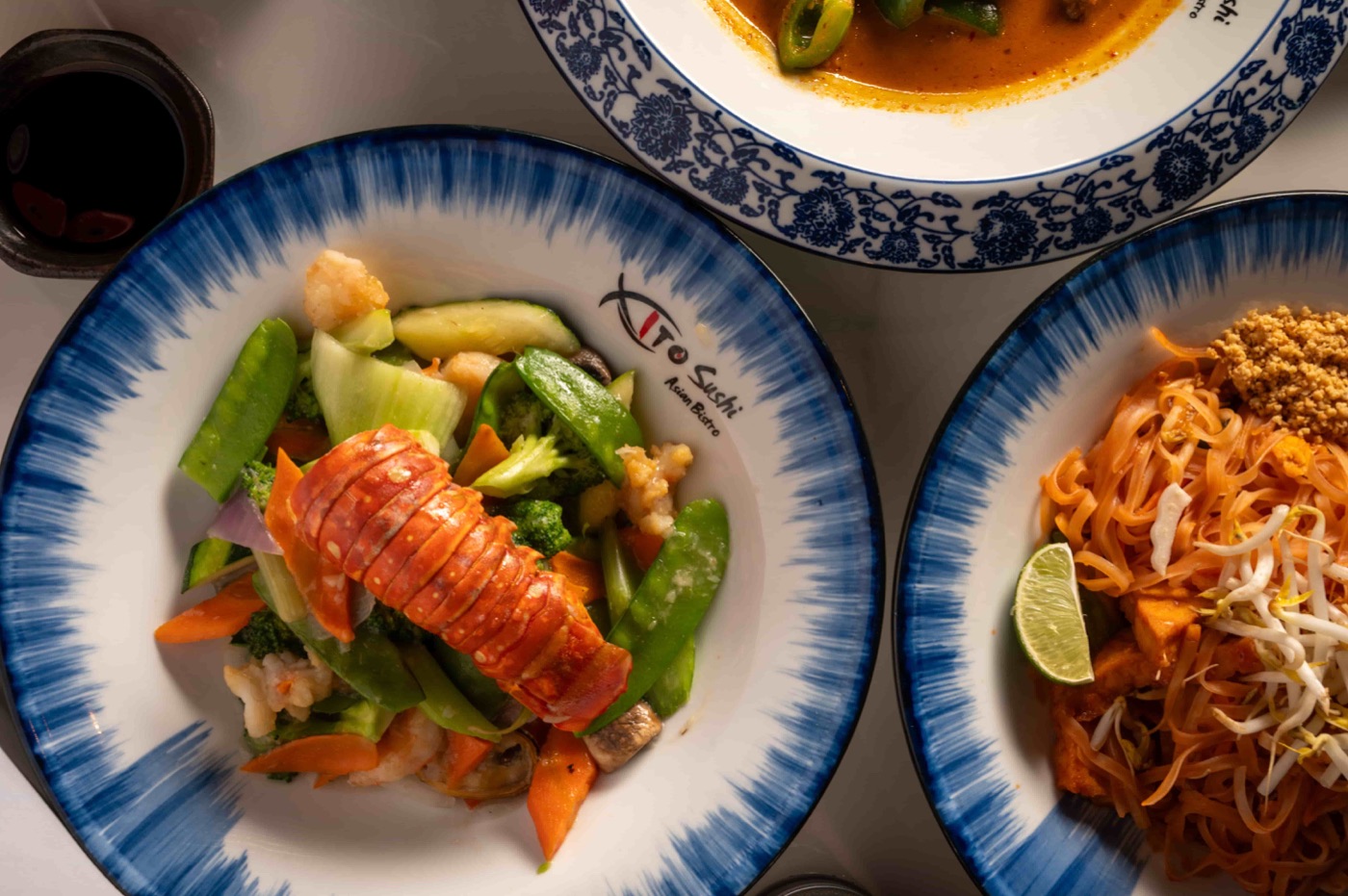 Overhead view of lobster tail with vegetables next to Pad Thai and Thai curry - East Moon Centennial CO